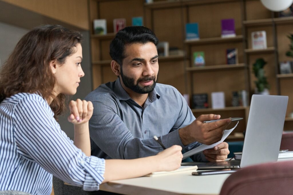 Indian teacher or mentor helping latin student, teaching intern using laptop.